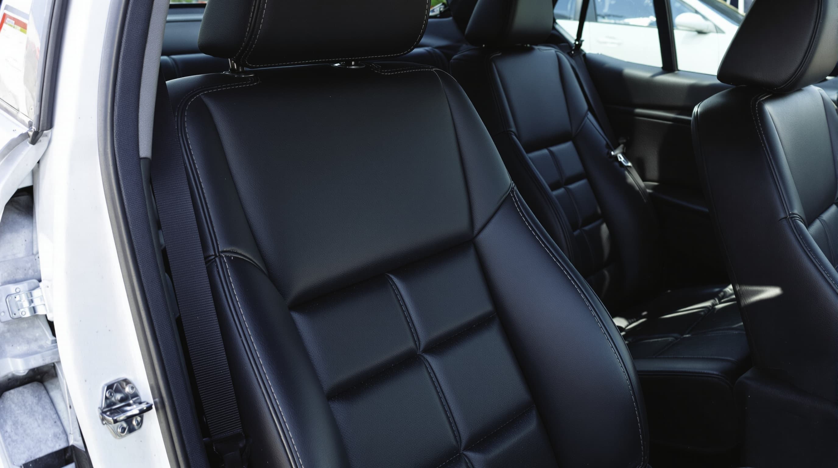 Spotless black leather front seats inside a car with the door open, crisp white contrast stitching, freshly cleaned in daylight