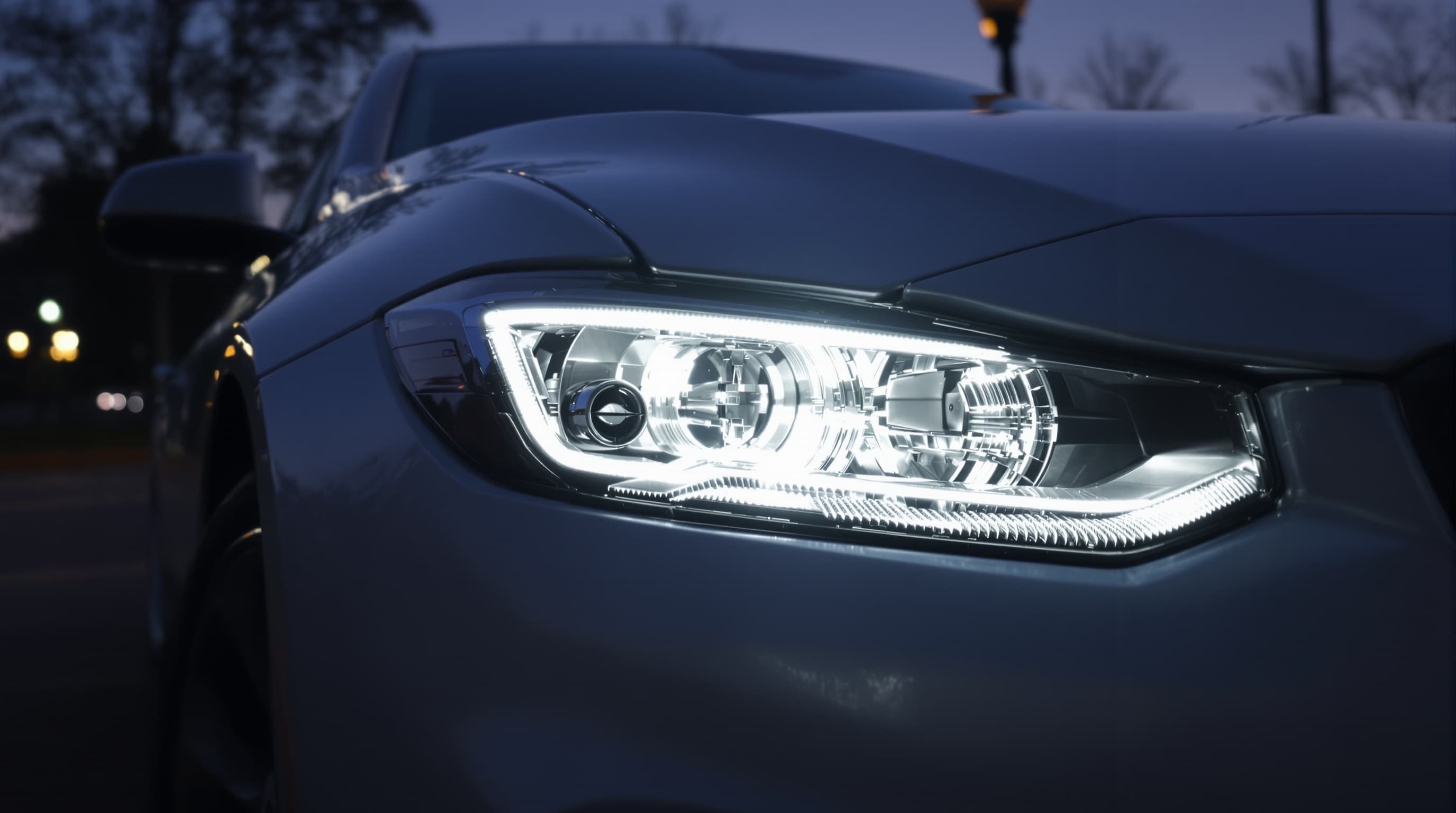 Three-quarter close-up of a bright white illuminated headlight on a clean modern car at dusk