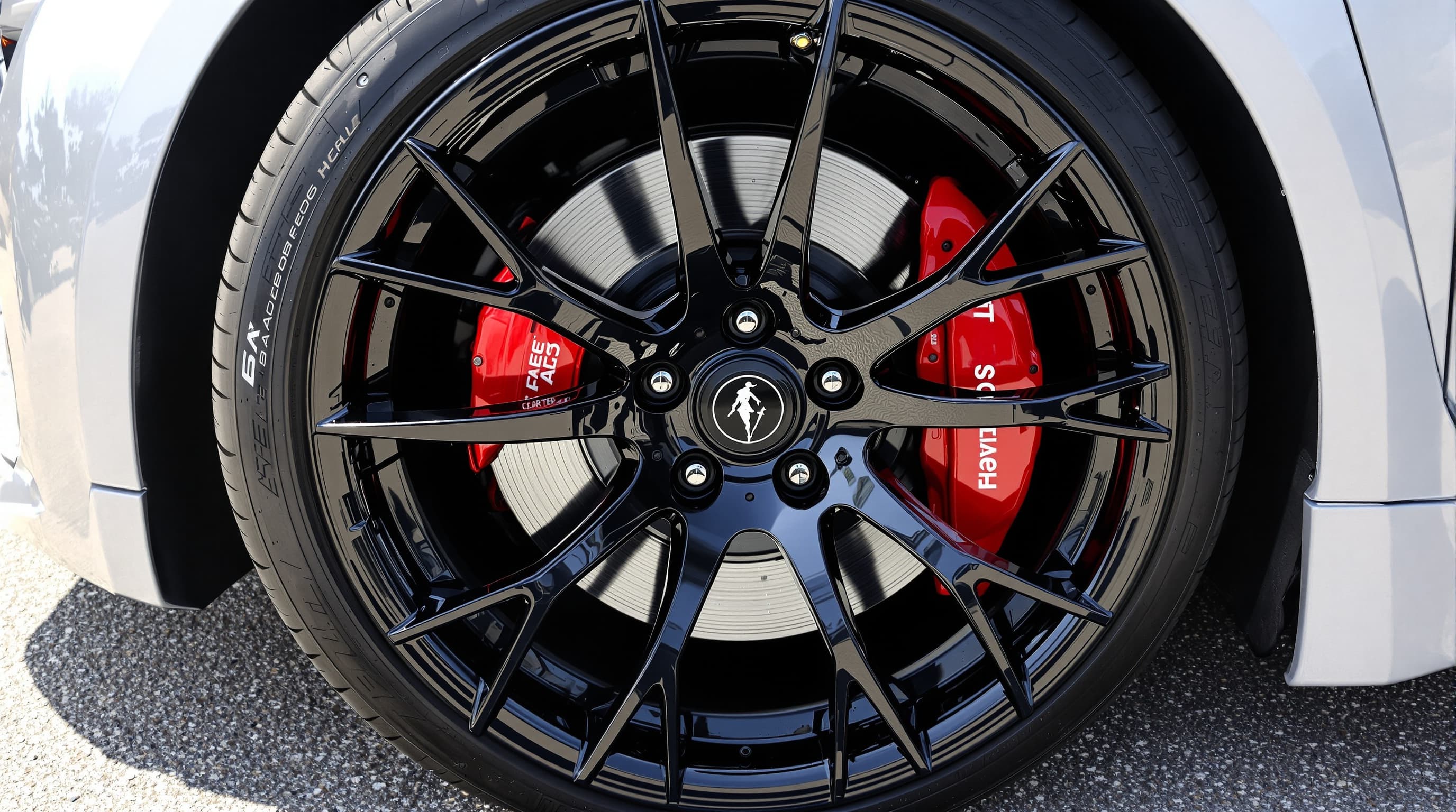 A clean gloss-black alloy wheel with a red brake caliper and glossy tire on a white sports car