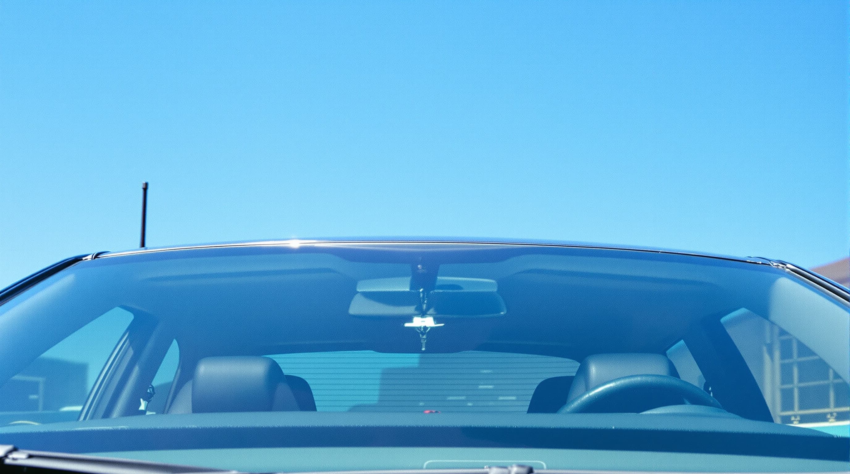 A spotless streak-free car windshield seen from the front, with a clear blue sky reflected in the clean glass