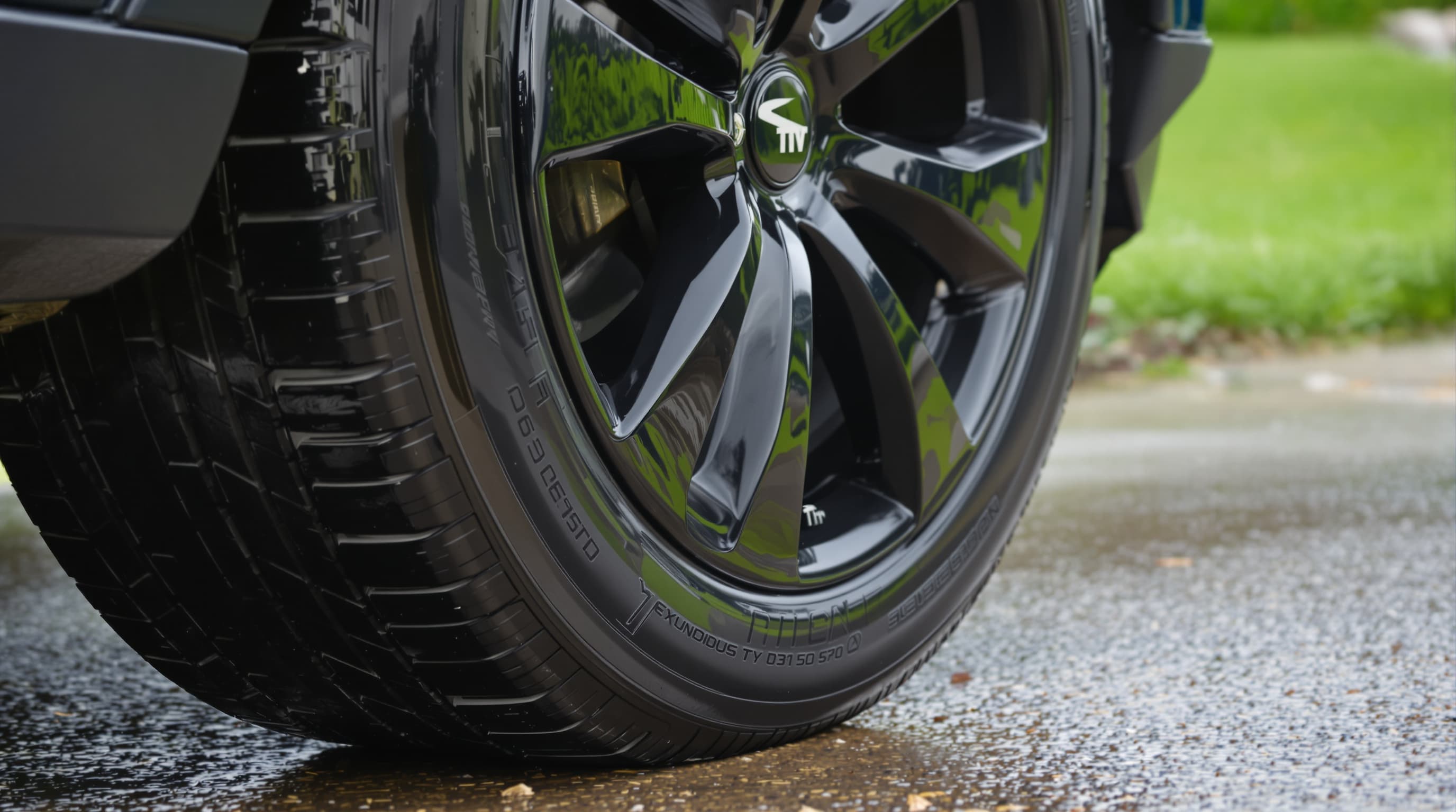 Low rear three-quarter close-up of a glossy wet-look black tire freshly dressed on a dark machined alloy wheel