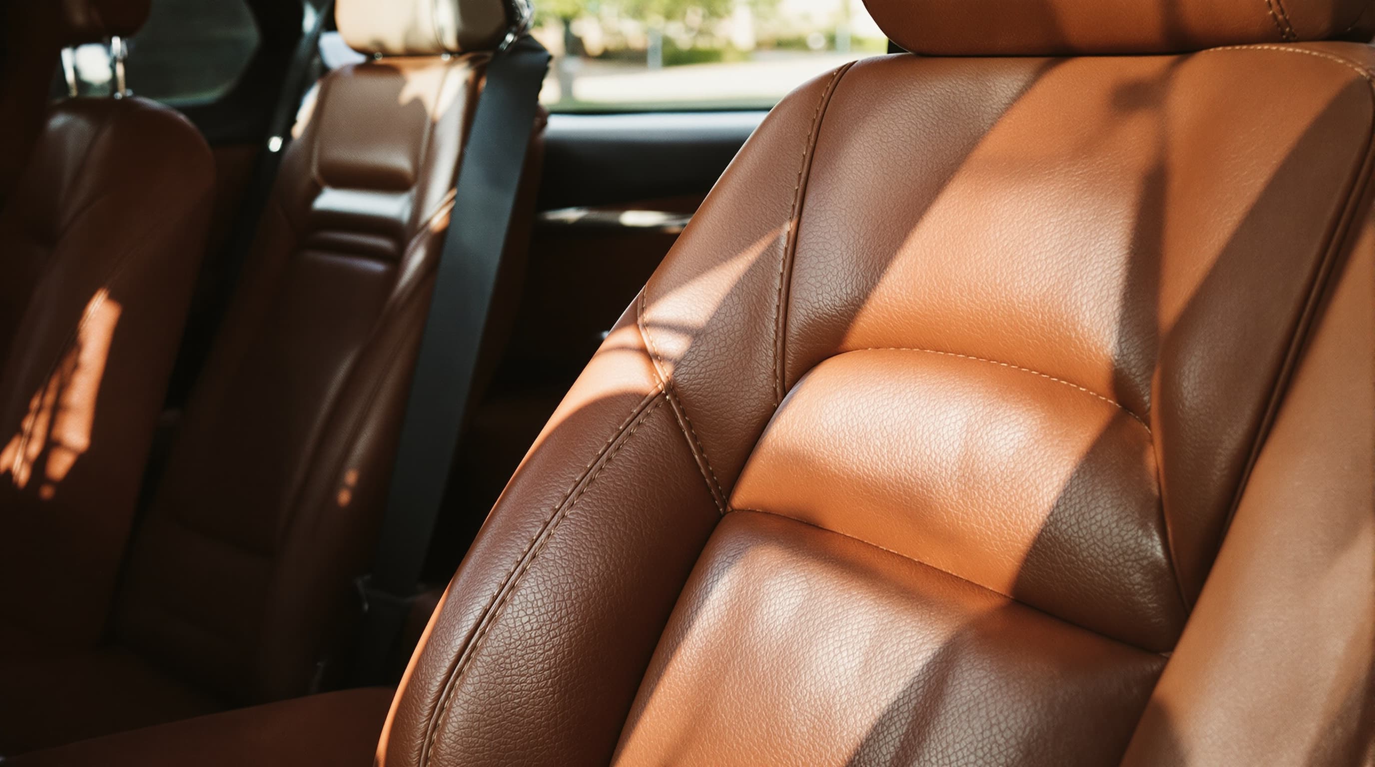 Rich cognac-brown leather car seats in warm afternoon sun streaming through the window, looking deeply conditioned and supple