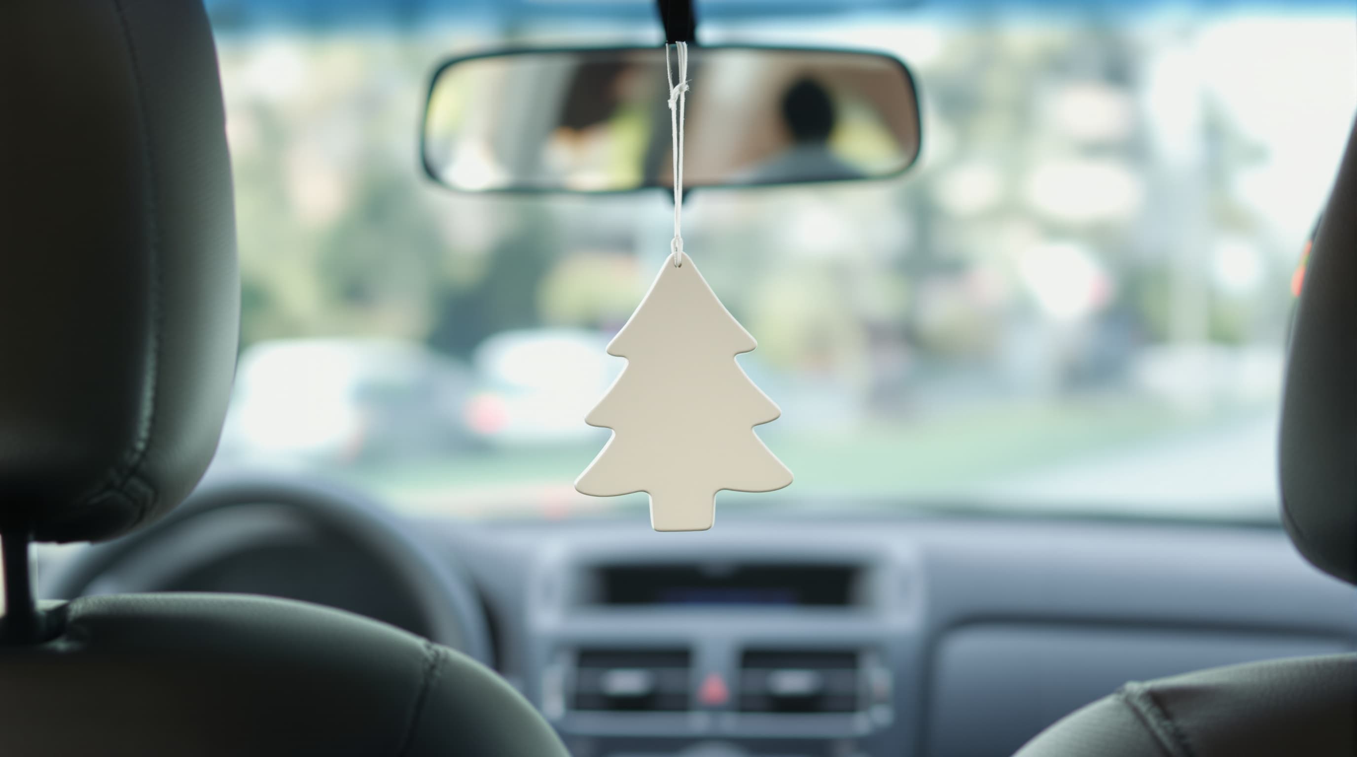 A plain tree-shaped air freshener hanging from a clean car's rearview mirror, the road ahead blurred through the windshield