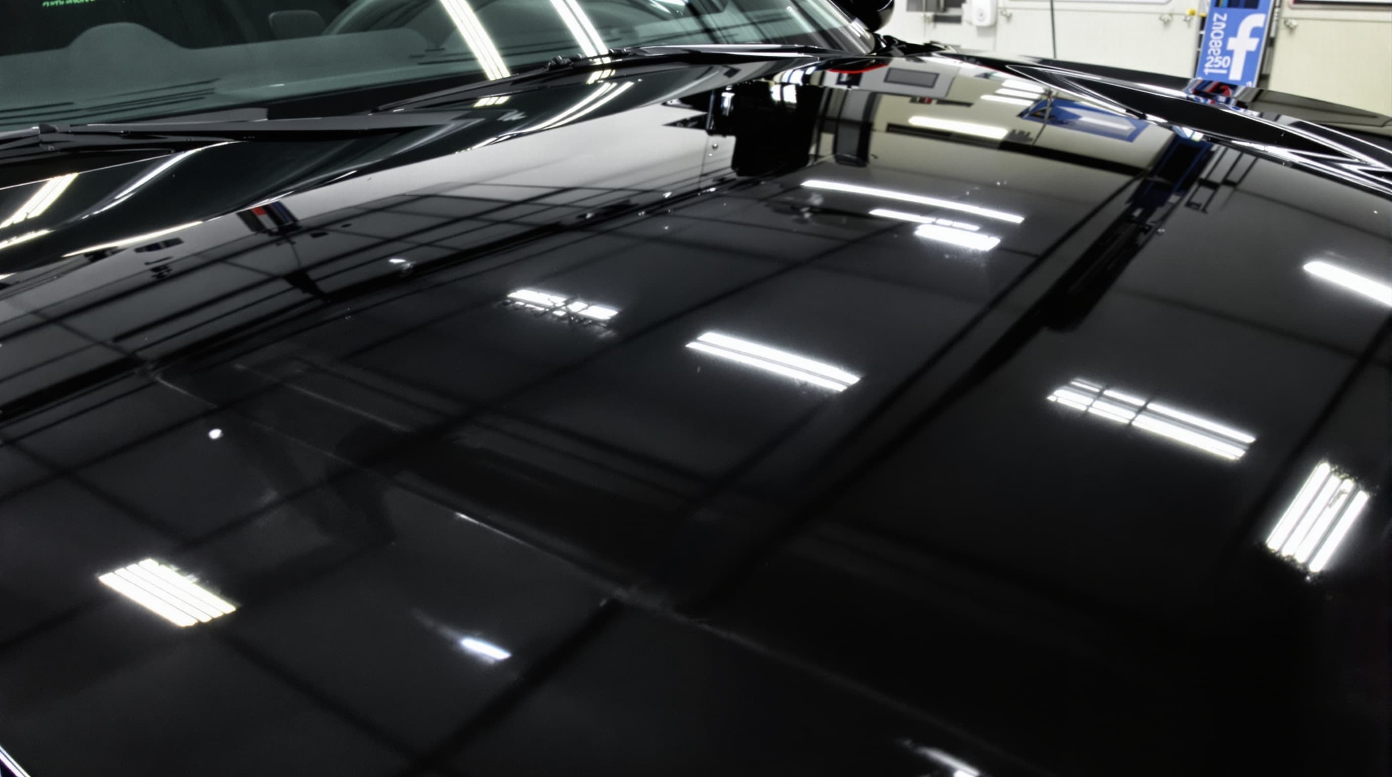 A flawless mirror-gloss black car hood reflecting overhead garage lights after polishing