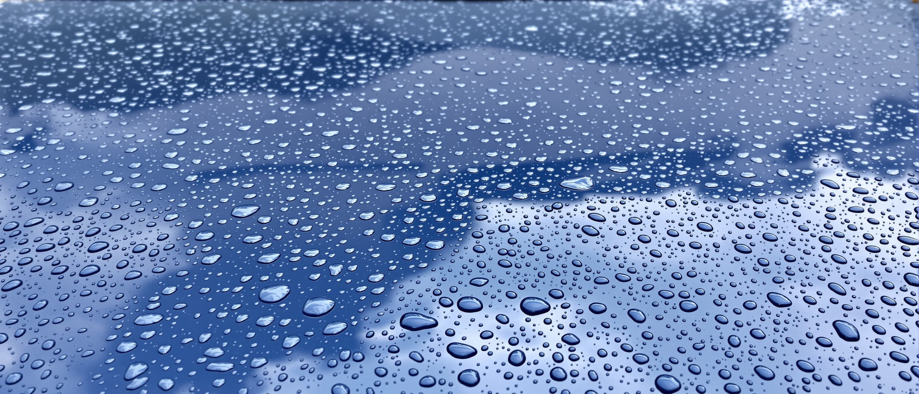 Tight water droplets beading across the glossy dark blue hood of a freshly treated car under overcast daylight